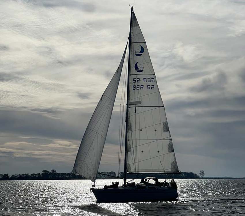 Ein Segelboot fährt mit Skipper und Crew auf einer Segelreise während des Urlaubs über das Wasser.